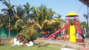 A playground with a yellow play structure, a red slide, and palm trees in the background. - Sealand Kihim (Alibag)