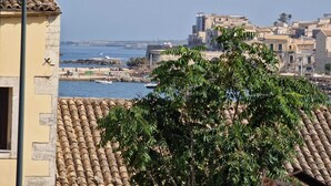 A coastal town with terracotta-tiled buildings, a rocky harbor, and a tree in the foreground. - The Golden House (Siracusa)