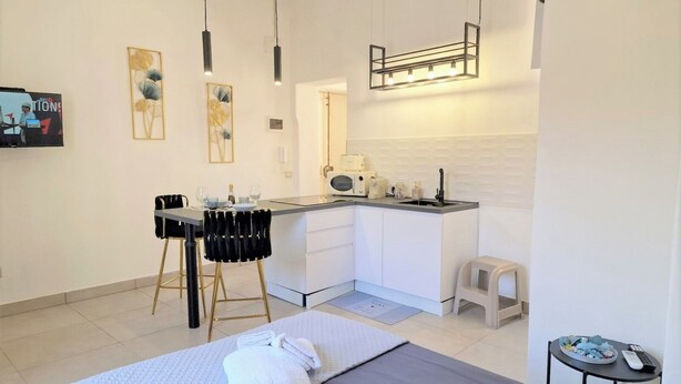 A modern hotel room with a bed, a small kitchenette, a dining area, and a bathroom. - The Golden House (Siracusa)