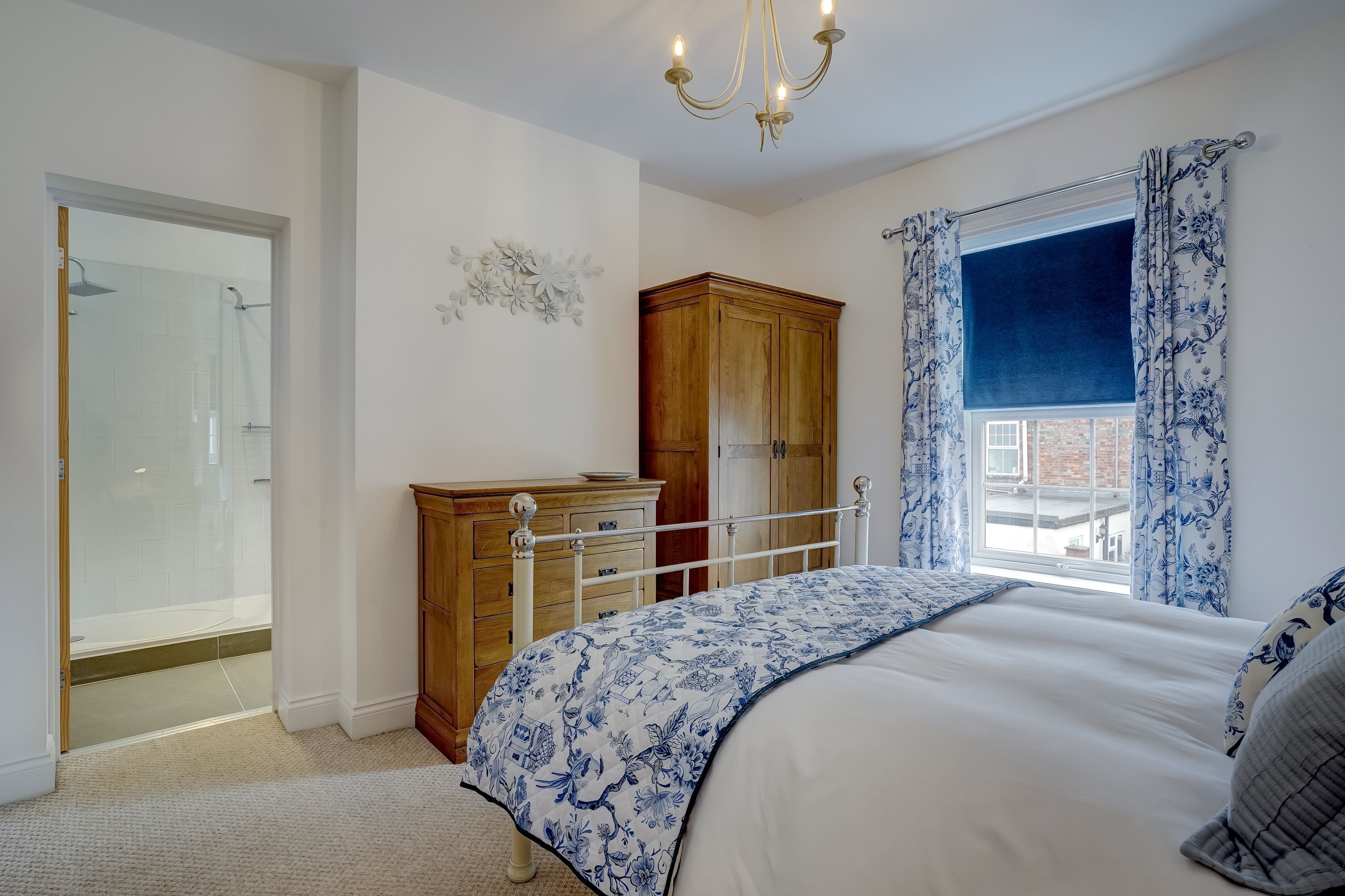 Une chambre à coucher comprenant un lit, une armoire en bois, une commode, un lustre et une fenêtre avec des rideaux.