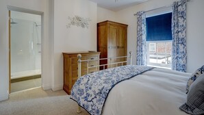 Une chambre à coucher comprenant un lit, une armoire en bois, une commode, un lustre et une fenêtre avec des rideaux.