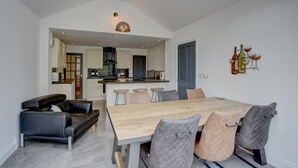 Une cuisine moderne dotée d’un îlot central, d’un coin repas avec une table en bois et des chaises rembourrées, ainsi que d’un canapé en cuir noir.