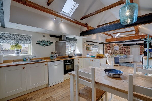 A spacious kitchen with wooden beams, a large window, and a dining area with a table and chairs.