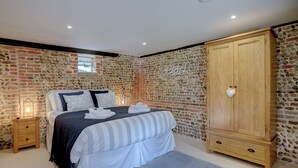 Un dormitorio con pared de piedra, un armario de madera, una cama con ropa de cama blanca y una mesita de noche con lámpara.