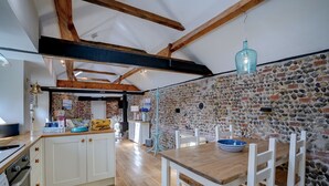 Una cocina con armarios blancos, una mesa de comedor de madera y una pared de piedra.