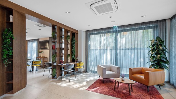 A modern living room with a sofa, armchair, and dining area with chairs and a table. - Hotel iNova (Zagreb)