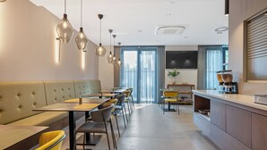 A modern dining area with a sofa, tables, chairs, pendant lights, a kitchen counter, and a TV. - Hotel iNova (Zagreb)