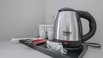 Una tetera de acero inoxidable sobre una bandeja con sobres de azúcar y bolsitas de té.