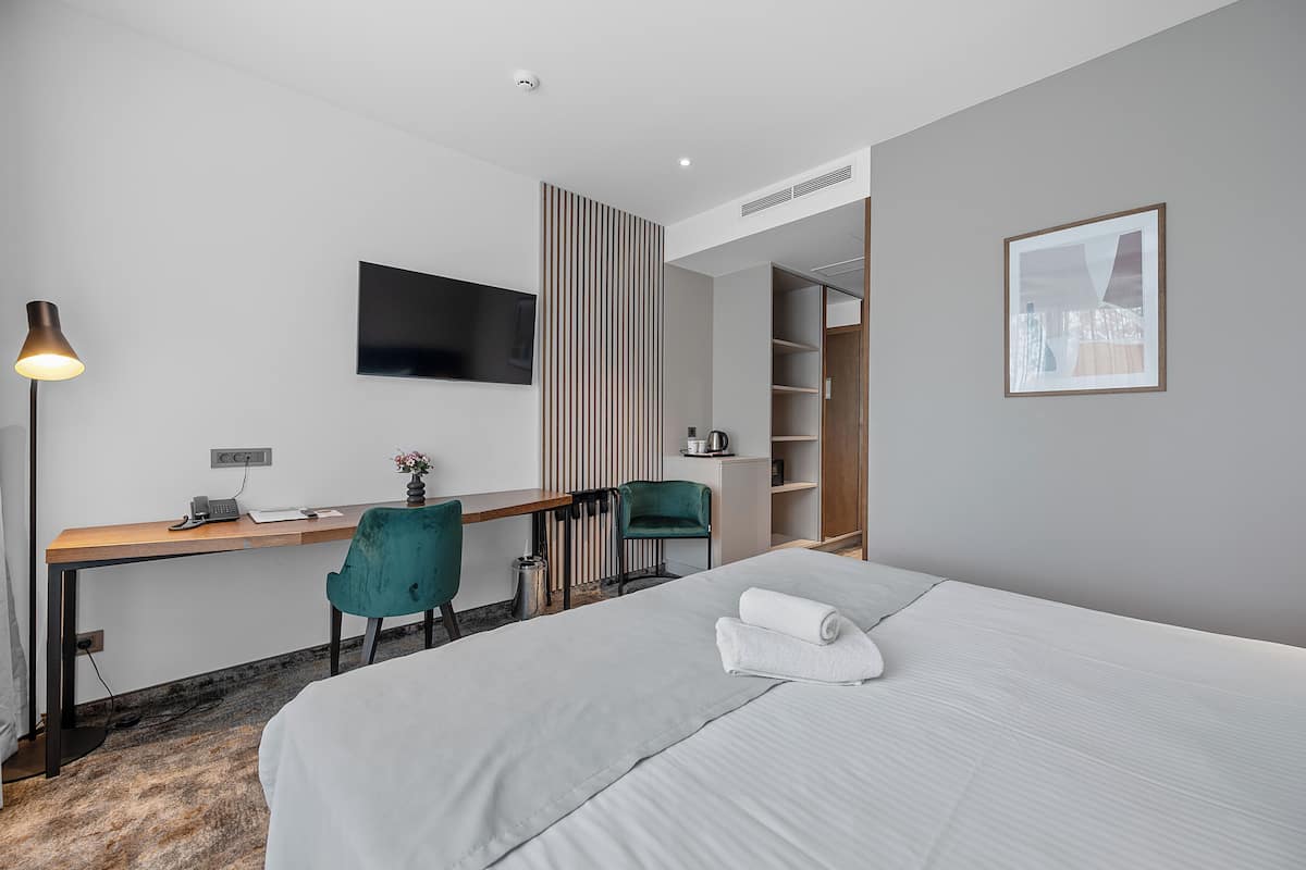 A modern hotel room with a bed, desk, chair, and a television.
