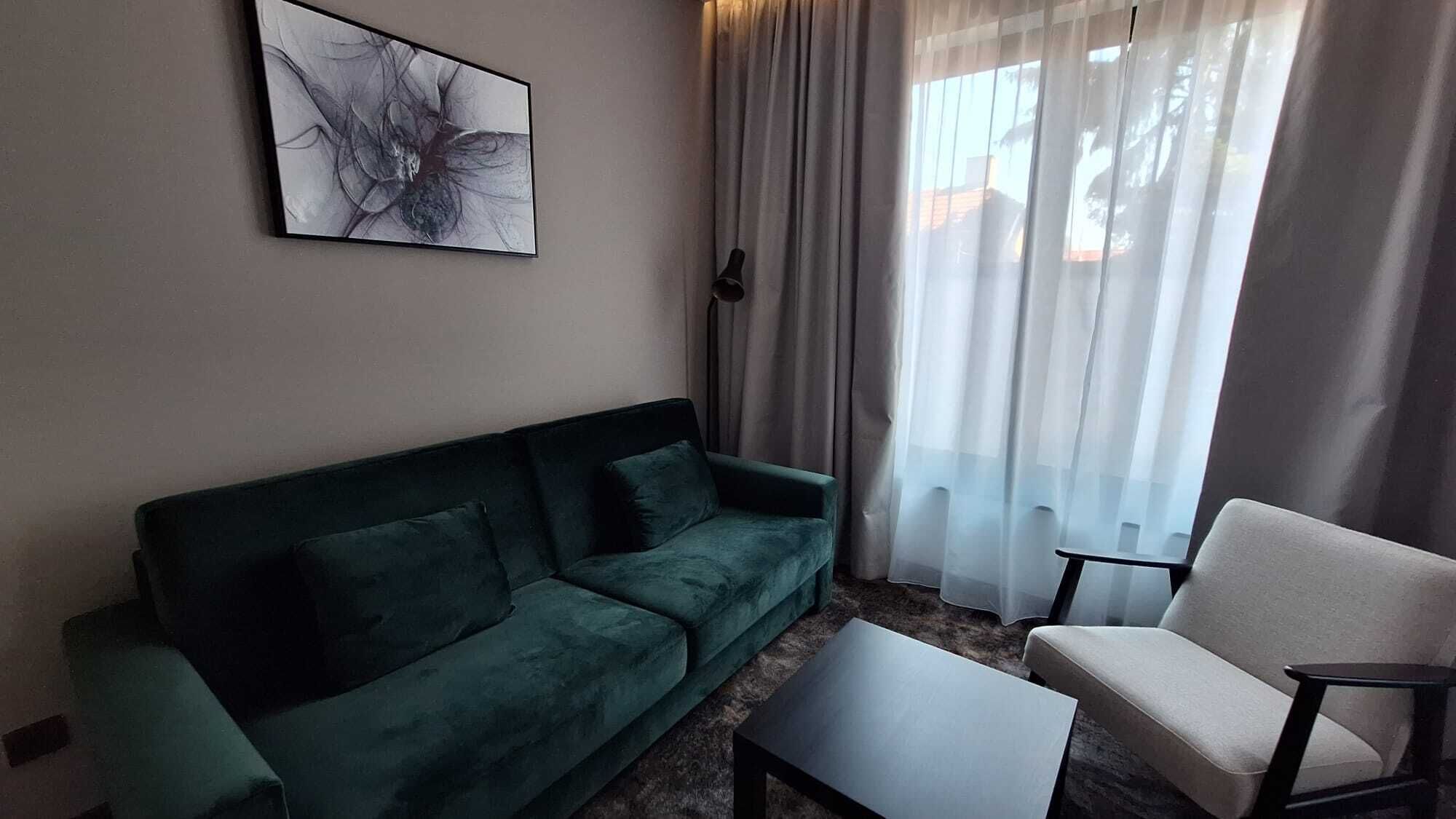 A living room with a dark green sofa, a white armchair, a coffee table, and a large abstract painting on the wall.