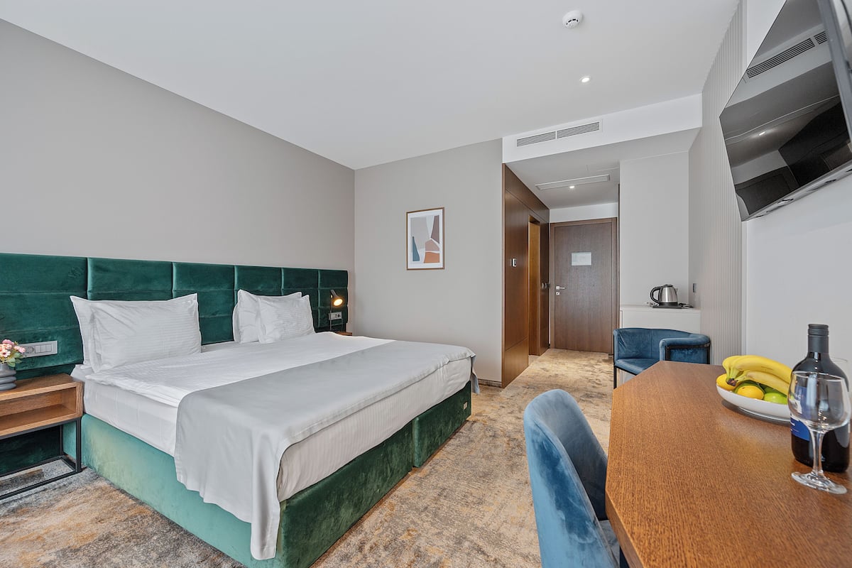 A hotel room with a bed, a dining table with a bottle and glass, and a chair.