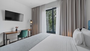A hotel room with a bed, a desk, a chair, a TV, and a window with curtains. - Hotel iNova (Zagreb)