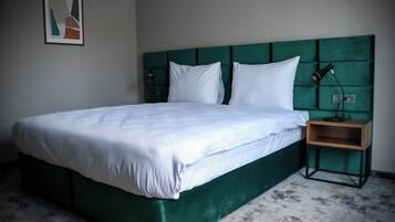 Un lit bien fait, avec une tête de lit recouverte d’un tissu vert, une table de chevet avec une lampe et un tableau encadré accroché au mur.