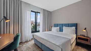 A hotel room with a large bed, a desk, a chair, and a window with curtains.
