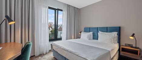 A hotel room with a large bed, a desk, a chair, and a window with curtains.