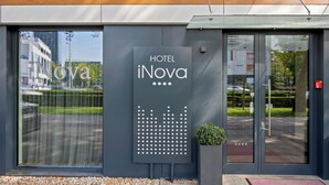 A modern hotel entrance with a large sign reading "HOTEL iNova" and a reflection of the surrounding area in the glass doors. - Hotel iNova (Zagreb)