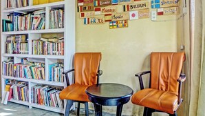 Ein Zimmer mit einer Bücherwand voller Bücher, zwei Ledersesseln, einem kleinen runden Tisch und einer Wand mit verschiedenen Nationalflaggen.