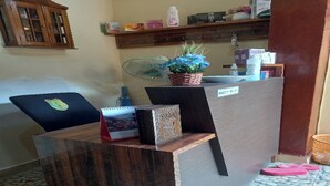 Un comptoir d’accueil avec un ordinateur portable, une plante en pot et un panneau indiquant un espace d’attente.