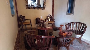 Un coin repas comprenant une table ronde et quatre chaises en bois, une petite table d’appoint et un miroir décoratif accroché au mur.
