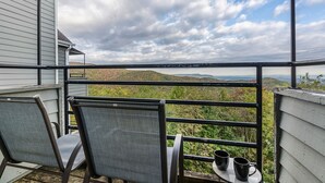 Een balkon met twee stoelen en een tafel, met uitzicht op een schilderachtig landschap met heuvels en een waterpartij.