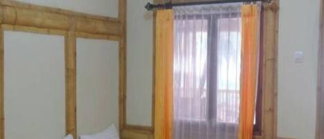 A room with two beds, wooden headboards, a window with curtains, and a wooden floor.