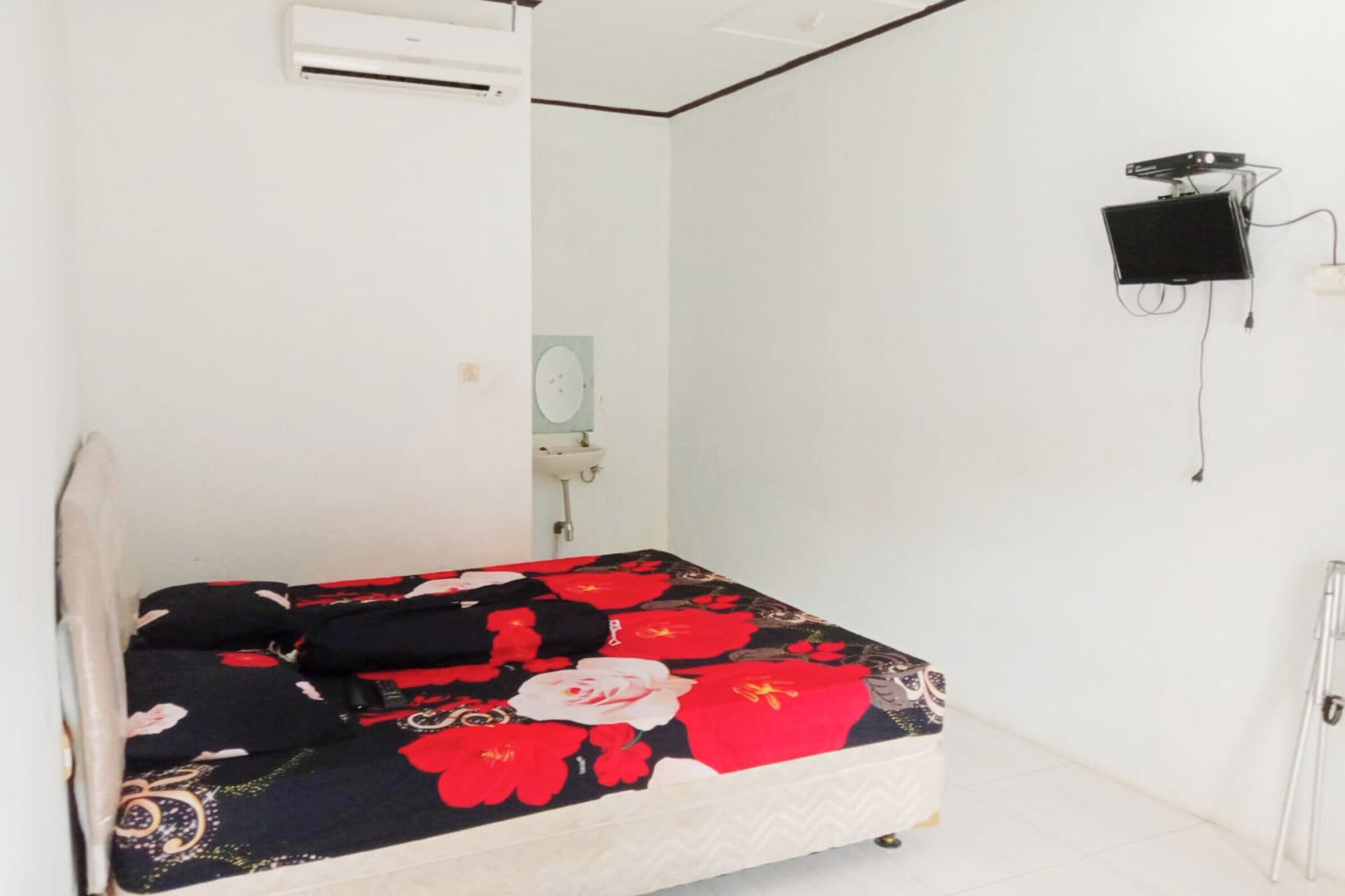 Una cama con una colcha estampada, una pared blanca, un lavamanos pequeño y un altavoz negro sujeto a la pared.