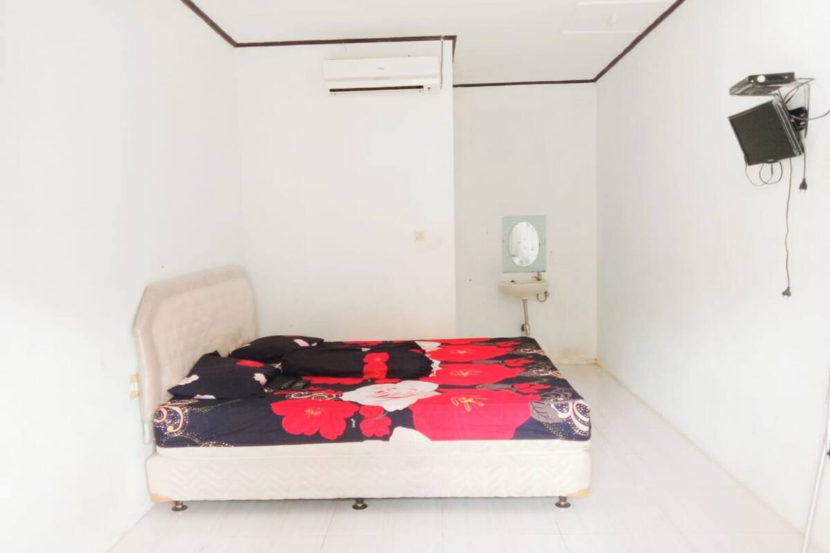 Ein kleines Zimmer mit einem Einzelbett, einer blumigen Bettdecke, einem weißen Kopfteil und einer Wandklimaanlage.
