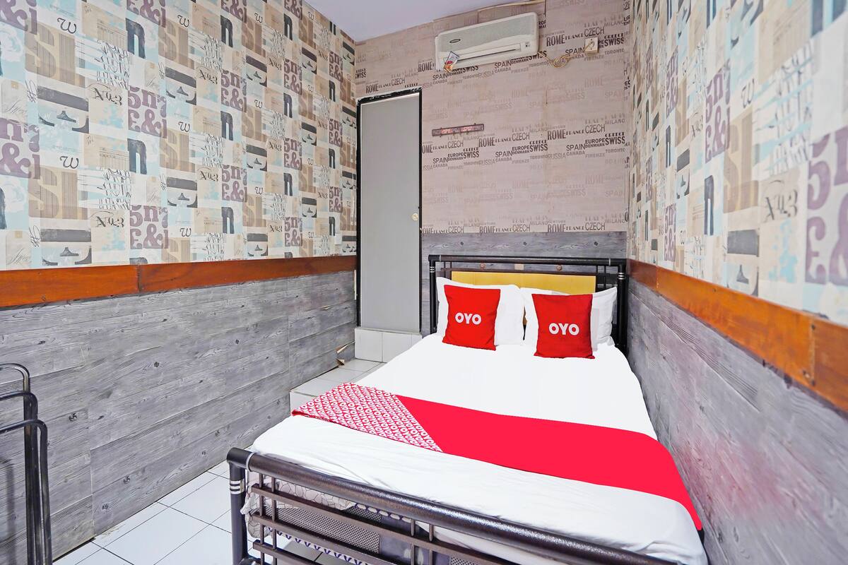 A small, narrow hotel room with a bed, a radiator, and a wall covered in printed text.