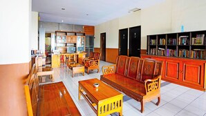 A spacious room with a wooden sofa, a dining table, and a bookshelf filled with books. - OYO 91415 De Wijaya Hotel (Sidoarjo)