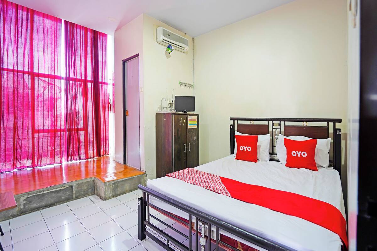 A hotel room with a bed, a wardrobe, a desk, and a window with curtains.