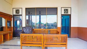 A spacious room with a large window, a wooden bench, and a black leather chair. - OYO 91415 De Wijaya Hotel (Sidoarjo)