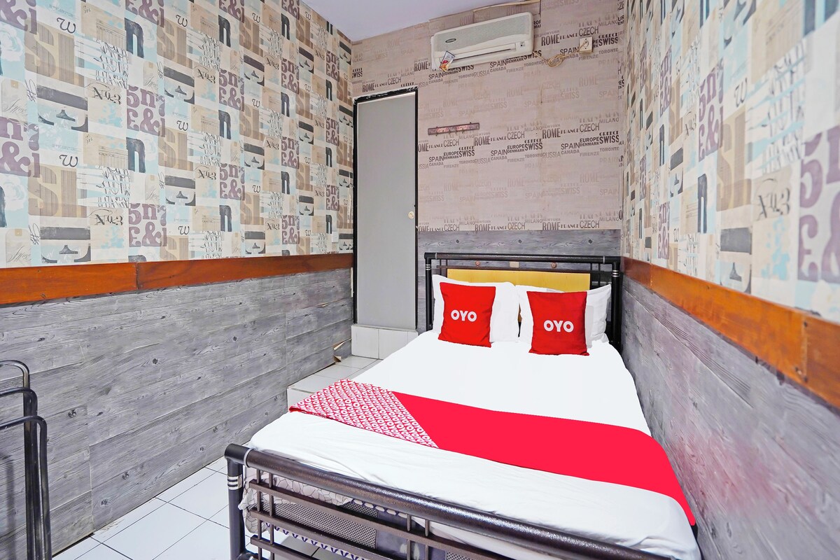 A small, narrow hotel room with a bed, a radiator, and a wall covered in printed text.