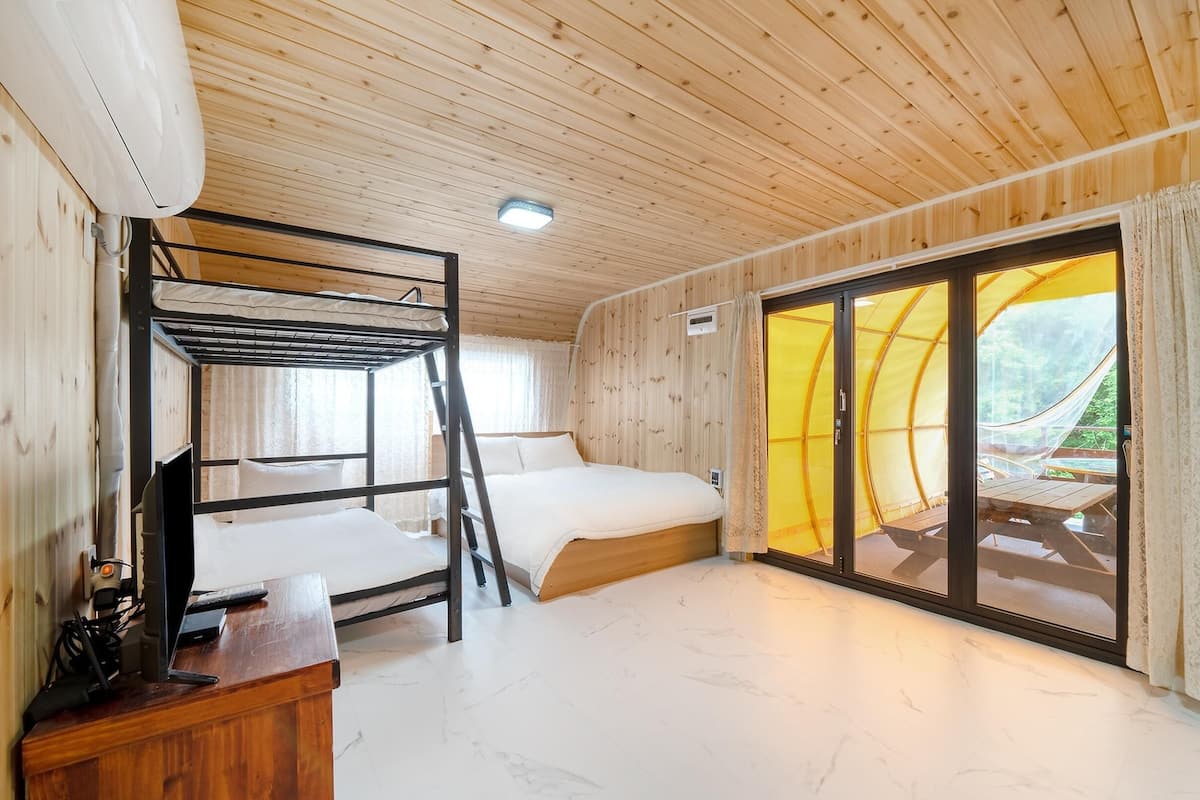 A wooden cabin room with bunk beds, a desk, and a sliding glass door leading to an outdoor area.