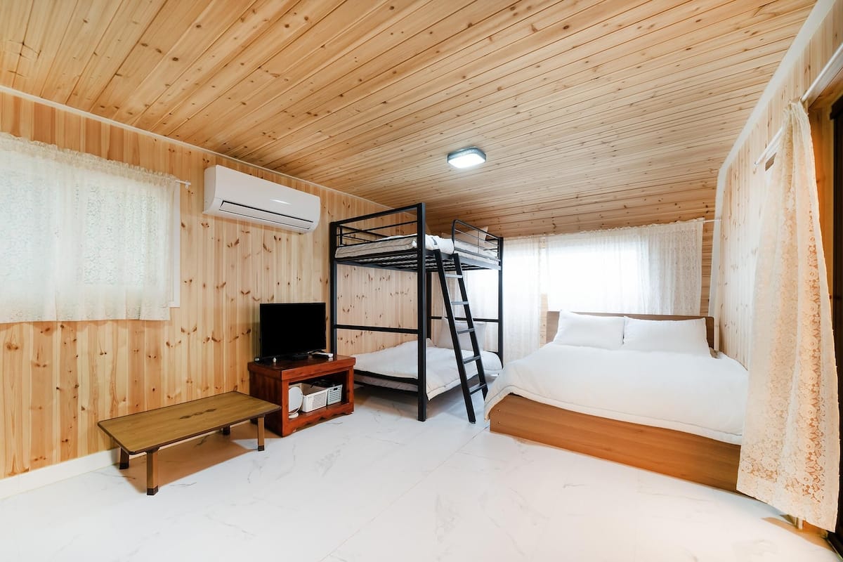 A wooden-paneled room with bunk beds, a television, a bench, and a small table.