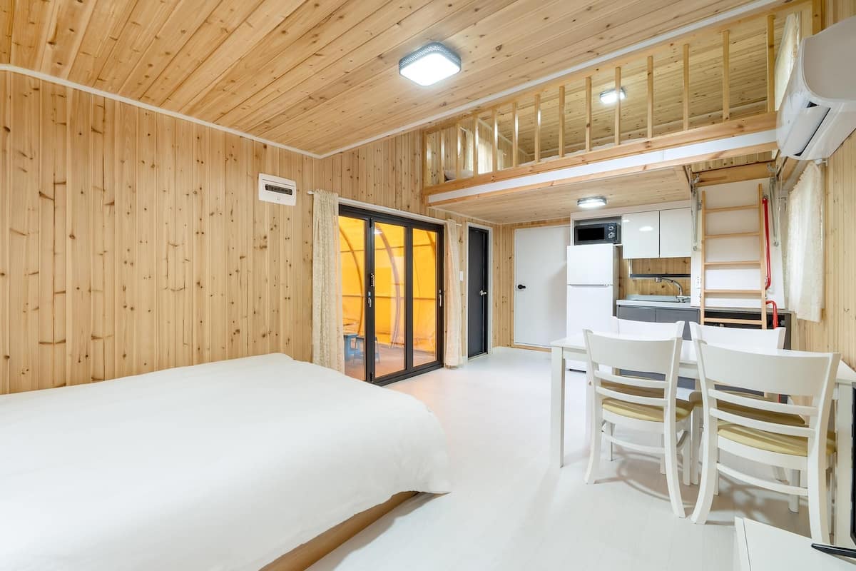 A wooden-paneled room with a bed, a dining table with chairs, and a kitchen area.