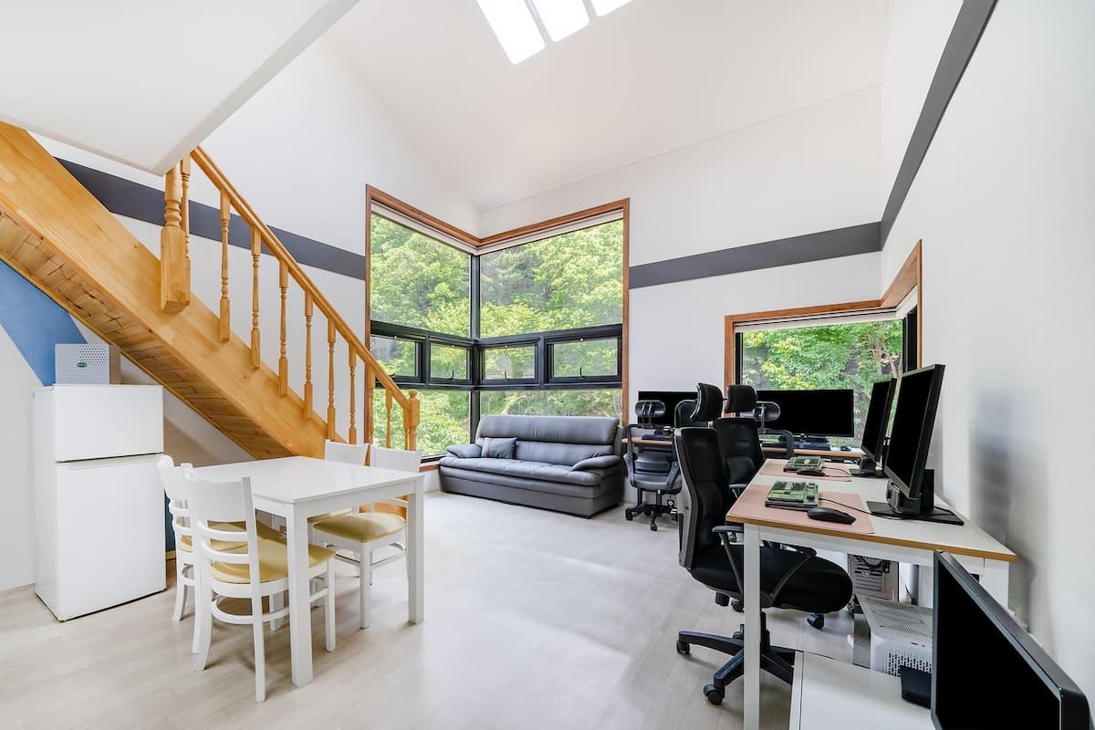 A modern office space with a wooden staircase, a white desk, a gray sofa, and a computer setup.