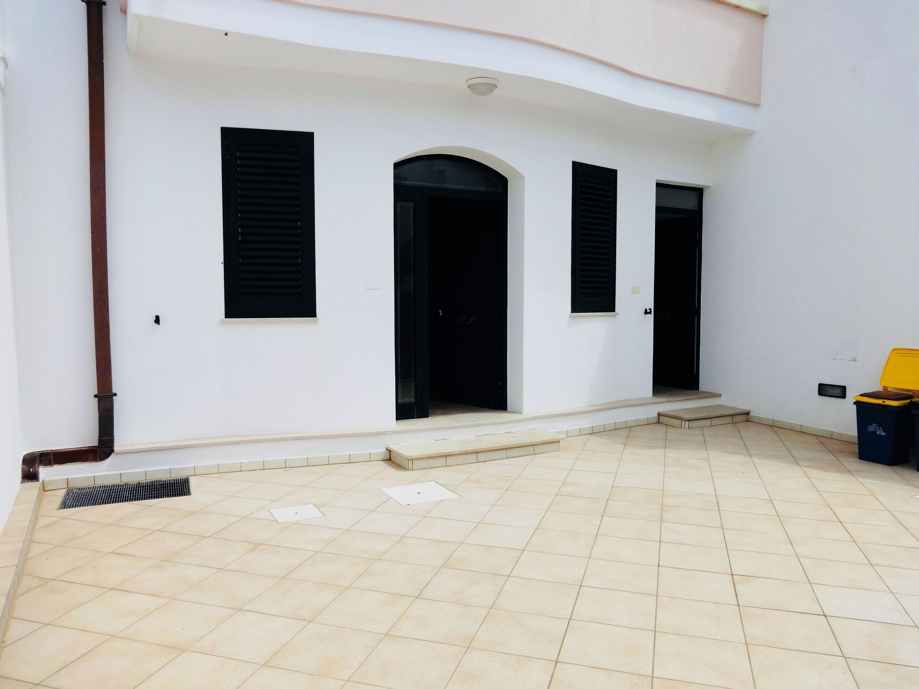 Un edificio blanco con tres puertas enmarcadas en negro y un patio adoquinado.