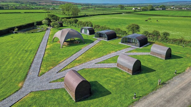 Un terrain de camping situé en zone rurale, doté de plusieurs tentes en forme de dôme et d’un pavillon central avec une table et des chaises.