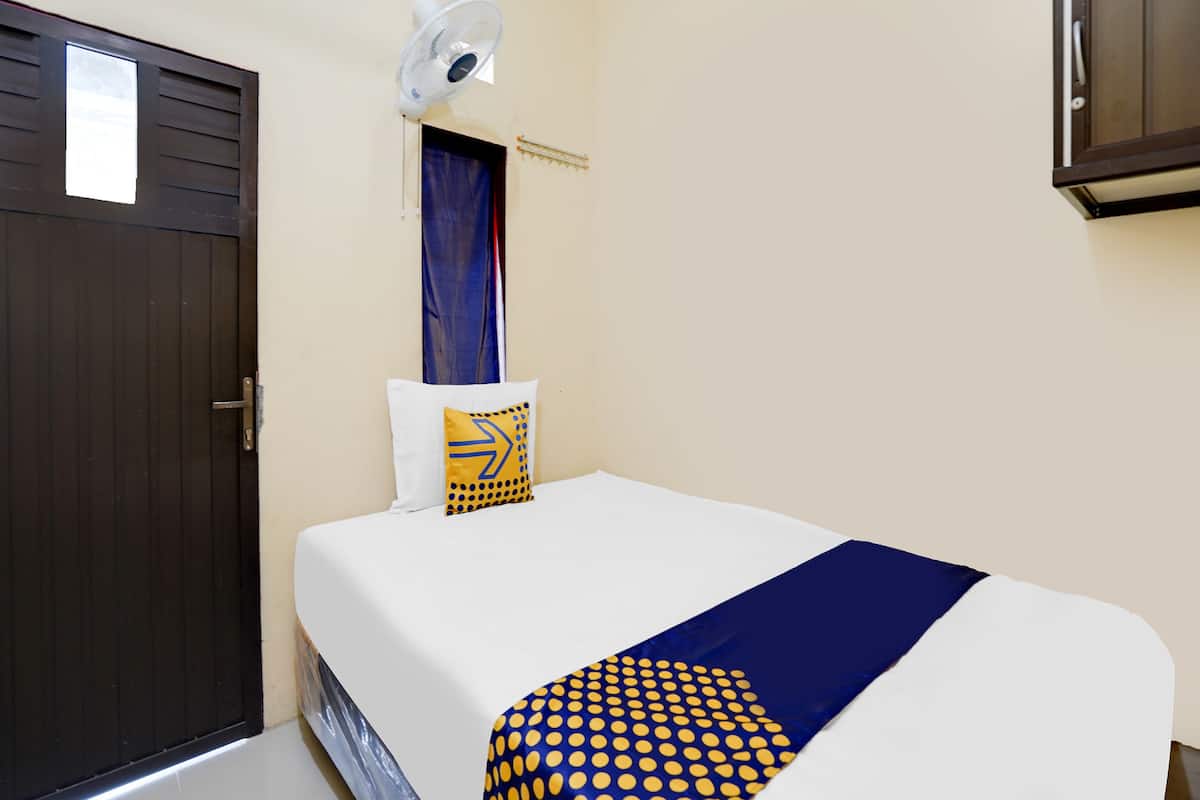 A hotel room with a bed, a wall-mounted fan, a door, and a curtain.