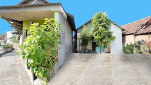 Une cour avec un chemin pavé, un bâtiment doté d’un toit en pente et un arbre au centre.