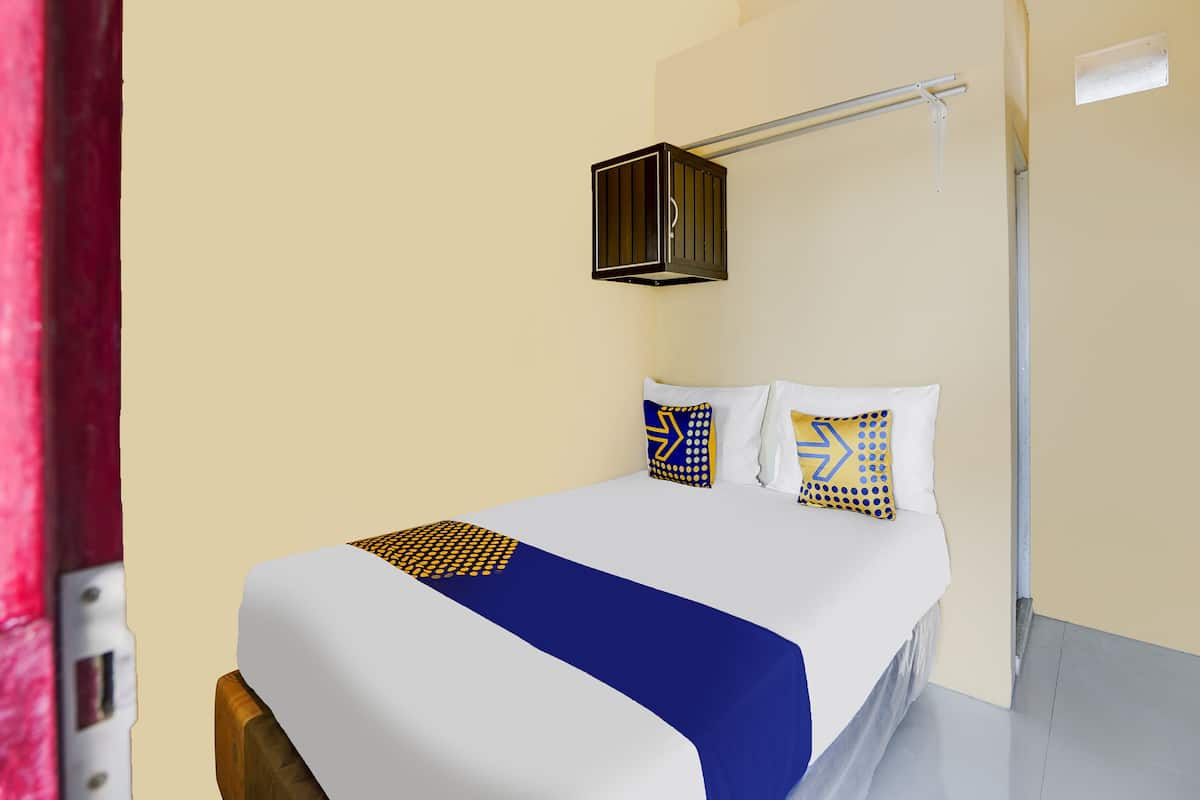 A hotel room with a bed, white walls, a red curtain, and a ceiling light fixture.
