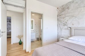 Un dormitorio con cama, mesita de noche, espejo y baño visible a través de una puerta abierta.