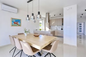 Una cocina moderna con una isla central, luces colgantes y un comedor con mesa y sillas de madera.