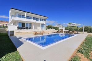 Una casa moderna de dos pisos con piscina, mobiliario exterior y cielo azul despejado.