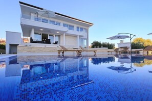 Una casa moderna de dos pisos con piscina, mobiliario exterior y sombrillas.