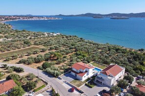 Una propiedad costera con un edificio blanco, una casa de techo rojo y vistas al mar y a un pueblo lejano.