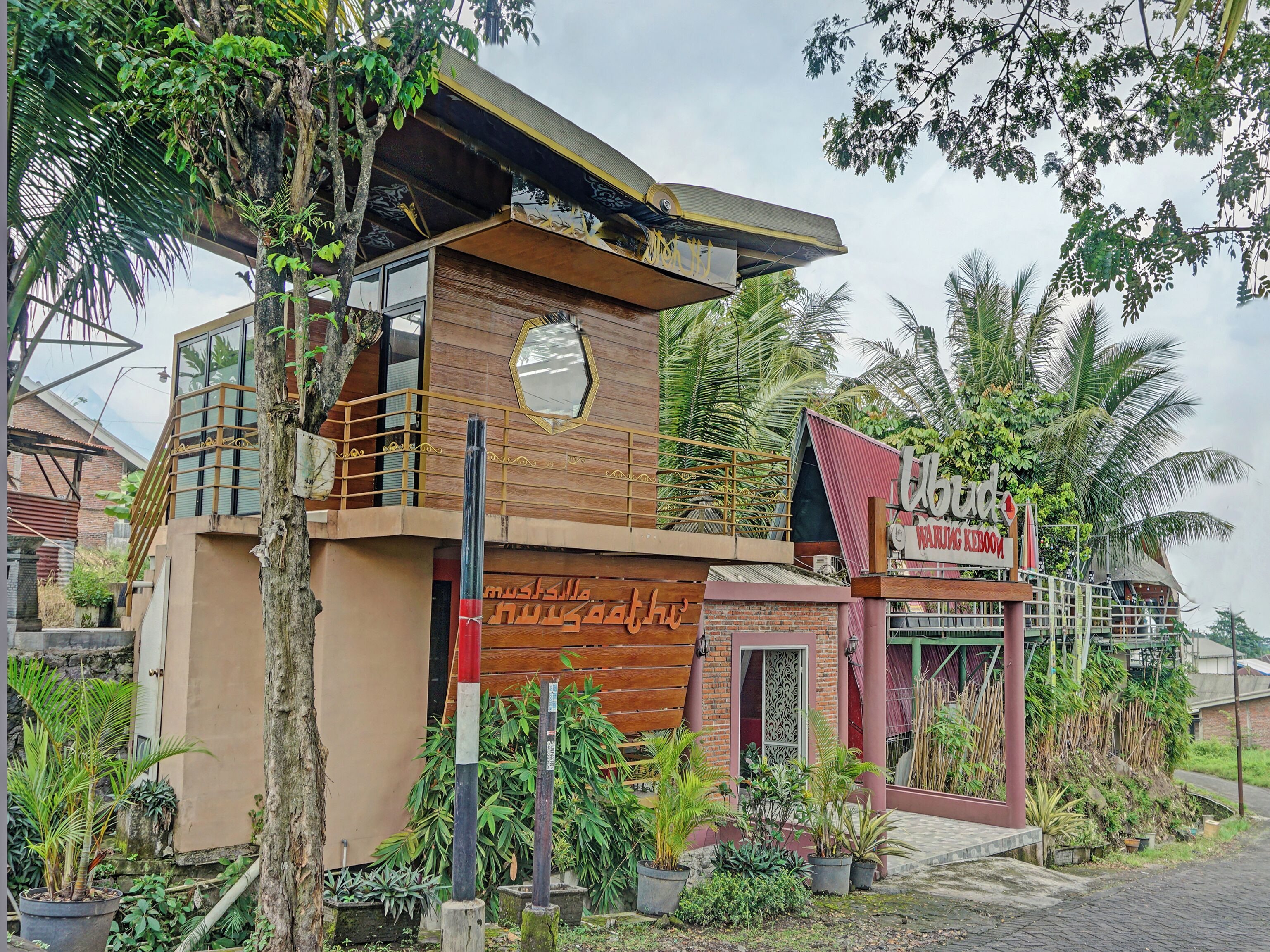 Um edifício com uma placa indicando "Warung Keroboka" e uma varanda com guarda-corpo.