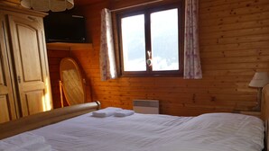 A wooden cabin room with a bed, a television on the wall, and a window with curtains. - Appartement Avec vue Panoramique sur la Vallée (Le Grand-Bornand)