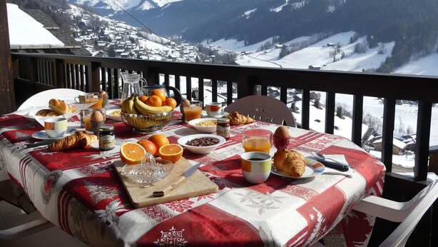 A breakfast table set with various food items and a view of snow-covered mountains. - Appartement Avec vue Panoramique sur la Vallée (Le Grand-Bornand)