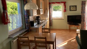 Ett kompakt kök med en matplats, en TV och ett fönster med gardiner.